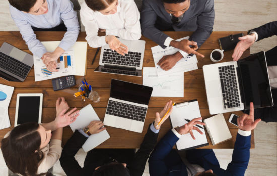 Business meeting. Busy people work in office, top view on wooden table with mobile phones, laptop, tablet and documents papers with diagram, corporate background